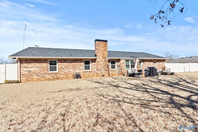 back of property with brick siding, a chimney, a shingled roof, and fence