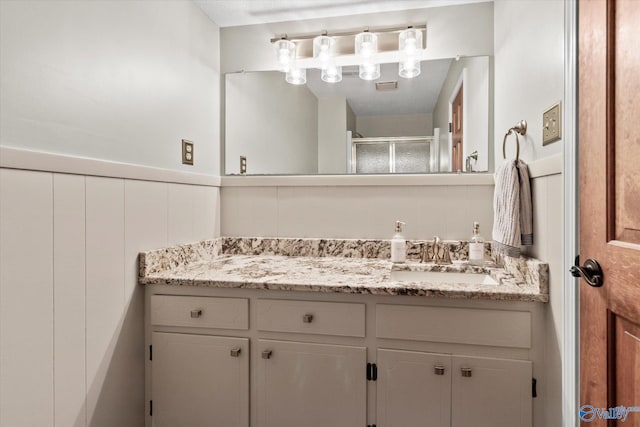 full bath featuring a wainscoted wall, a shower stall, visible vents, and vanity