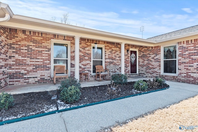 doorway to property featuring covered porch and brick siding