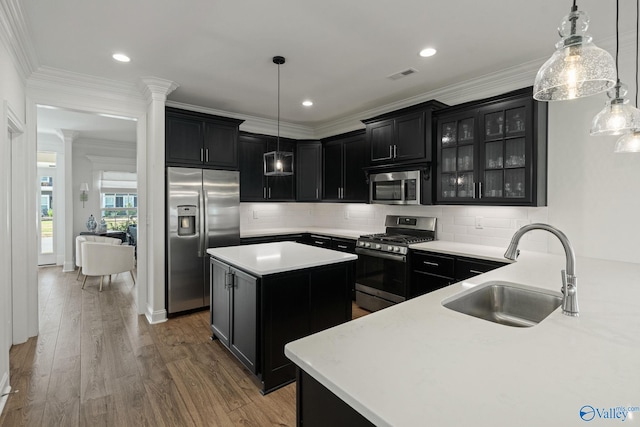 kitchen with appliances with stainless steel finishes, sink, decorative columns, wood-type flooring, and a kitchen island