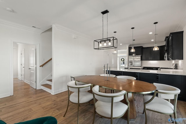 kitchen with decorative light fixtures, stainless steel appliances, wood-type flooring, decorative backsplash, and ornamental molding