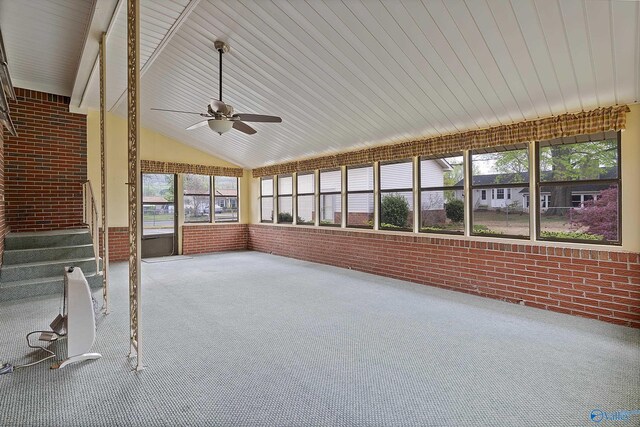 unfurnished sunroom with brick wall, a ceiling fan, vaulted ceiling with beams, and carpet