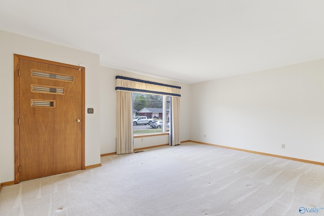 spare room featuring light carpet and baseboards