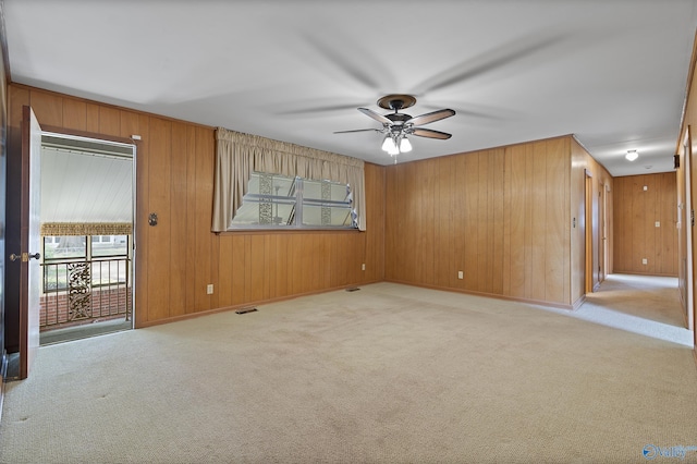 carpeted empty room with wooden walls, baseboards, a ceiling fan, and visible vents