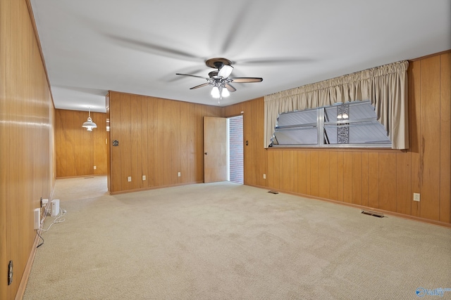 carpeted spare room with wooden walls, visible vents, and a ceiling fan