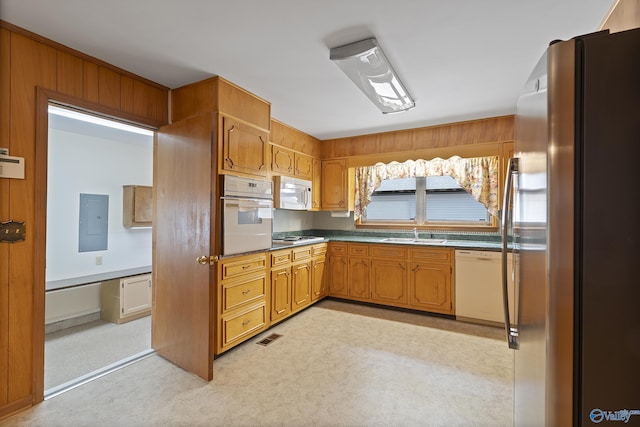 kitchen with a sink, white appliances, electric panel, brown cabinetry, and light colored carpet