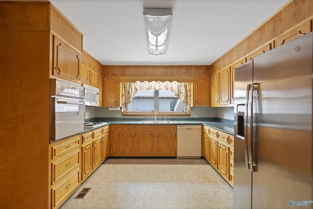 kitchen featuring a sink, dark countertops, visible vents, white appliances, and brown cabinetry