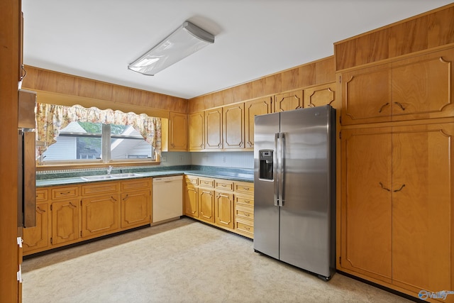 kitchen featuring a sink, dark countertops, white dishwasher, brown cabinets, and stainless steel refrigerator with ice dispenser