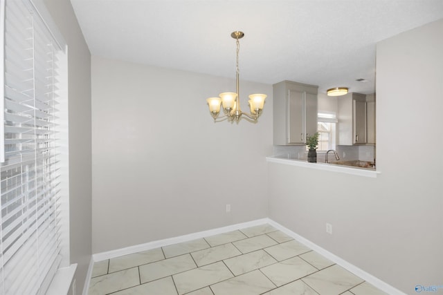 unfurnished dining area featuring a chandelier, a sink, and baseboards