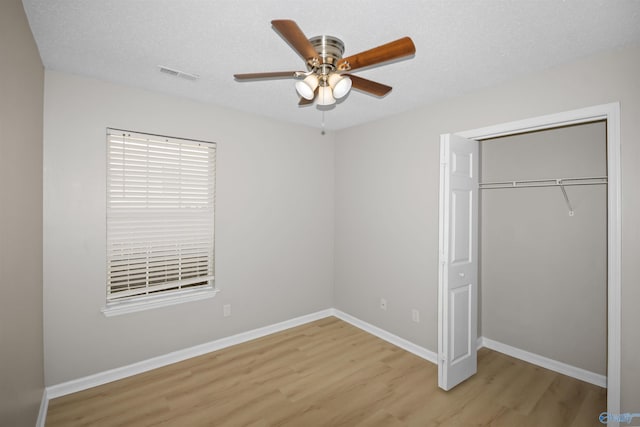 unfurnished bedroom with a closet, a textured ceiling, visible vents, and wood finished floors