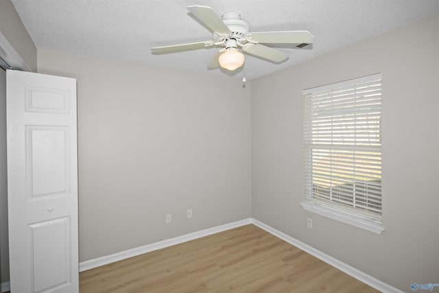 empty room with light wood-style flooring, a textured ceiling, baseboards, and a ceiling fan