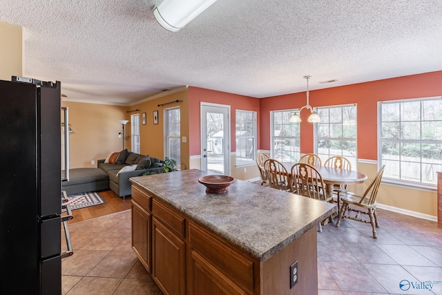 kitchen with pendant lighting, brown cabinets, freestanding refrigerator, open floor plan, and a kitchen island