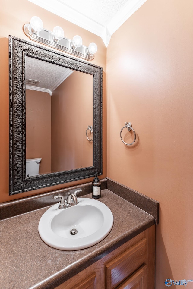 half bathroom with toilet, visible vents, vanity, and crown molding