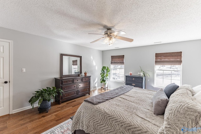 bedroom featuring dark wood-style floors, a textured ceiling, baseboards, and a ceiling fan