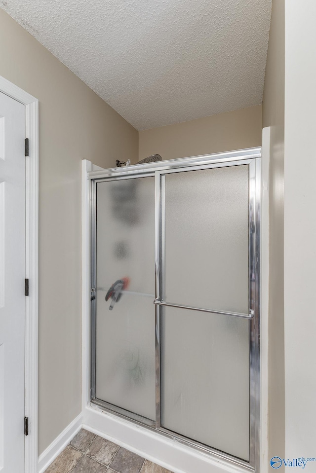 bathroom with baseboards, a textured ceiling, and a shower with shower door