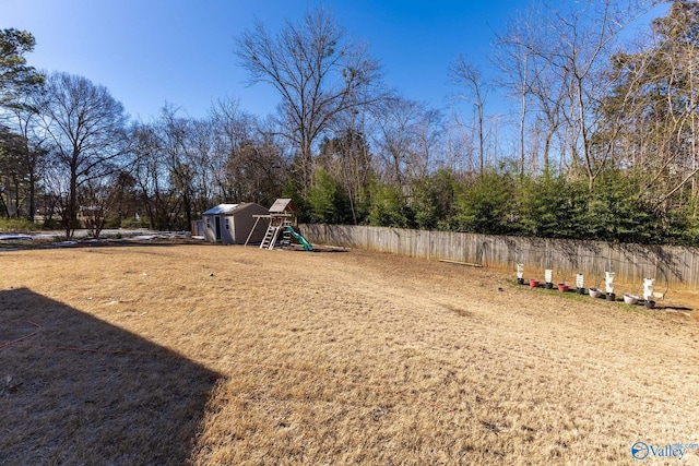 view of yard with a storage shed, fence, a playground, and an outdoor structure