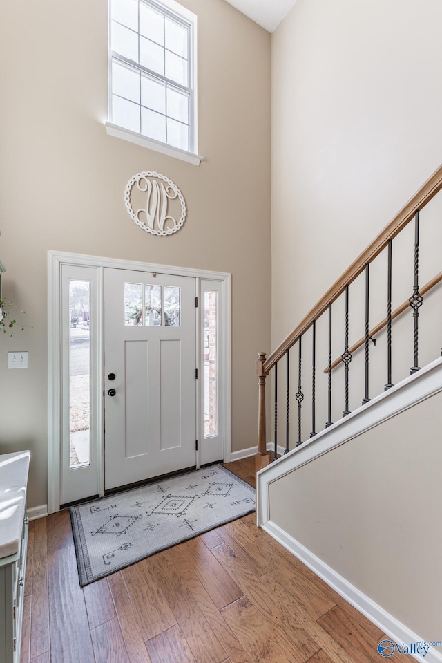 foyer featuring stairs, hardwood / wood-style flooring, a towering ceiling, and baseboards