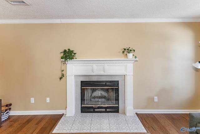 details featuring visible vents, a tiled fireplace, ornamental molding, wood finished floors, and baseboards