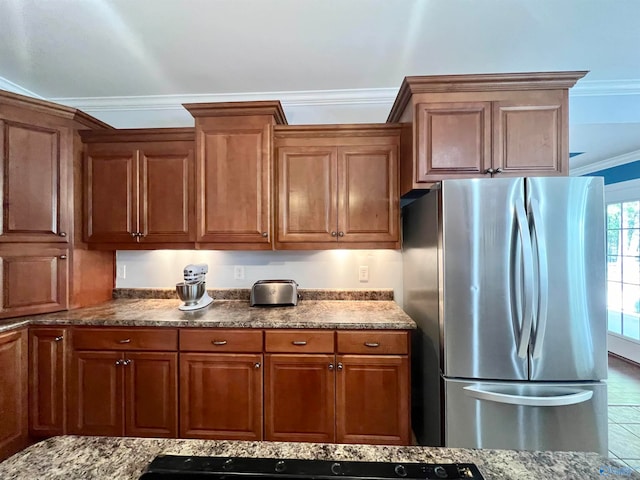 kitchen featuring light stone countertops, stainless steel fridge, tile patterned flooring, and ornamental molding