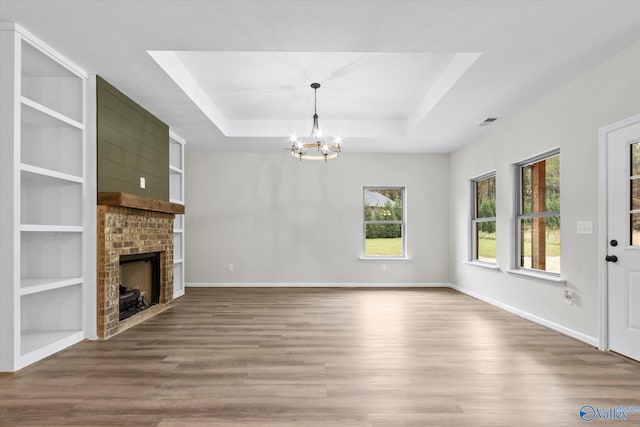 unfurnished living room with wood-type flooring, a raised ceiling, built in features, a fireplace, and a chandelier