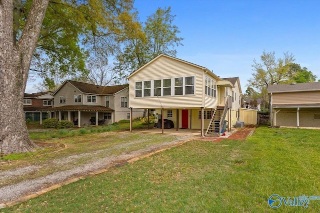 back of house featuring dirt driveway, stairs, a yard, a carport, and a patio