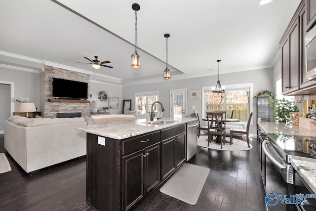 kitchen featuring dark brown cabinetry, a kitchen island with sink, sink, pendant lighting, and a fireplace