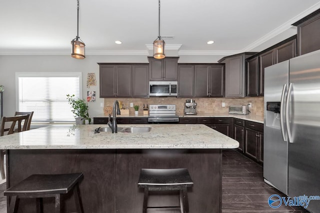 kitchen featuring appliances with stainless steel finishes, ornamental molding, sink, pendant lighting, and an island with sink