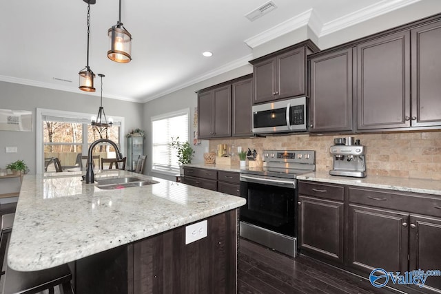 kitchen with tasteful backsplash, stainless steel appliances, sink, decorative light fixtures, and a center island with sink