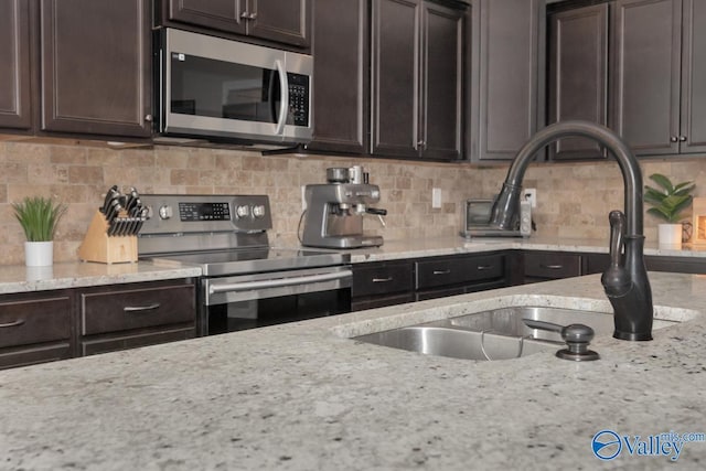 kitchen with decorative backsplash, appliances with stainless steel finishes, light stone counters, dark brown cabinets, and sink