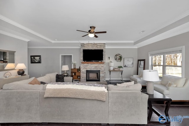 living room featuring ceiling fan, a stone fireplace, ornamental molding, and a tray ceiling