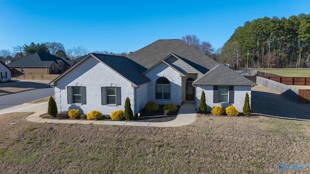 french provincial home featuring brick siding, roof with shingles, a front lawn, and fence