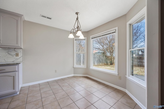 unfurnished dining area with light tile patterned flooring, visible vents, an inviting chandelier, and baseboards