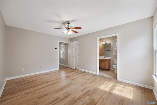 unfurnished bedroom with a sink, ensuite bath, light wood-style floors, baseboards, and ceiling fan