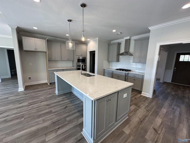 kitchen with dark wood-style flooring, gray cabinets, appliances with stainless steel finishes, a sink, and wall chimney range hood