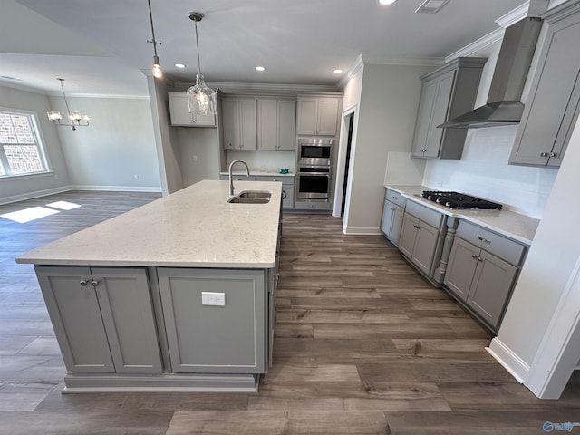 kitchen with gray cabinetry, appliances with stainless steel finishes, a sink, an island with sink, and wall chimney exhaust hood