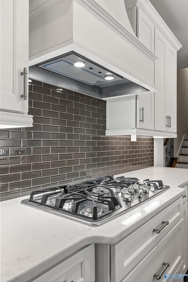 kitchen with white cabinetry, decorative backsplash, stainless steel gas cooktop, custom range hood, and light stone counters