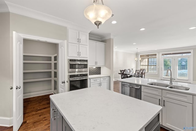 kitchen with white cabinetry, stainless steel appliances, sink, hanging light fixtures, and ornamental molding