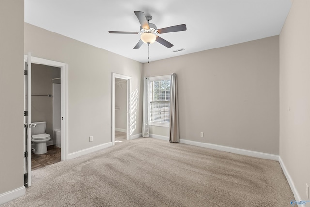 unfurnished bedroom featuring a spacious closet, ceiling fan, carpet floors, ensuite bath, and a closet