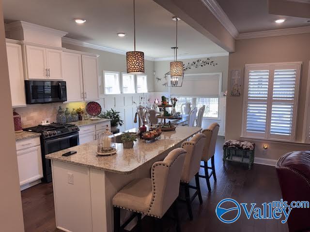 kitchen featuring light stone countertops, black appliances, white cabinetry, a kitchen breakfast bar, and tasteful backsplash