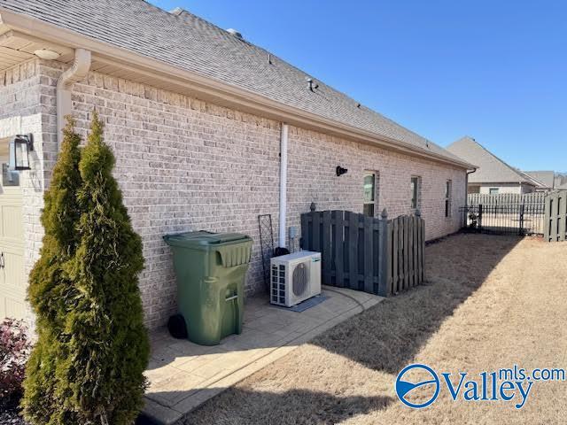 view of property exterior with ac unit, brick siding, a shingled roof, and fence