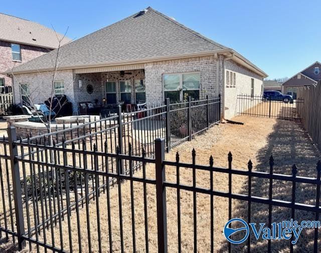 exterior space with brick siding, roof with shingles, a fenced backyard, and a patio area