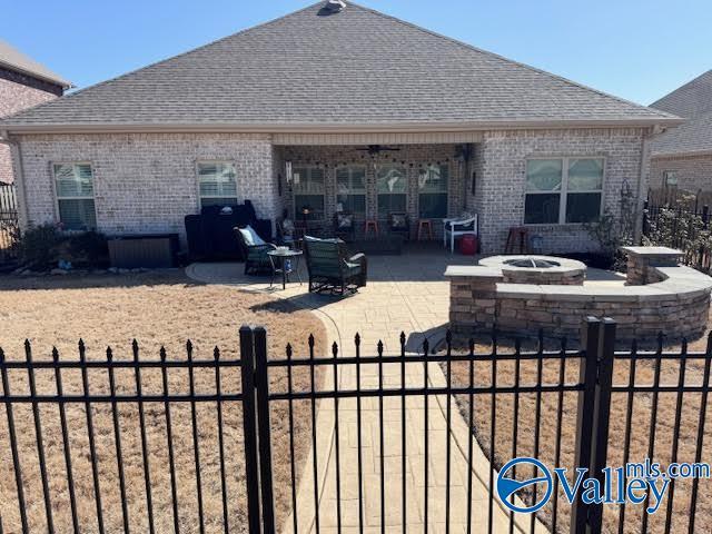 back of house with a fenced front yard, brick siding, roof with shingles, and an outdoor fire pit