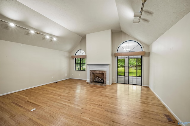 2211 Pumpkin Center Rd NE, Fort Payne, AL 35967 - unfurnished living room with light wood finished floors, rail lighting, a textured ceiling, a brick fireplace, and baseboards