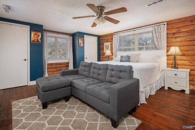 bedroom with a textured ceiling, dark hardwood / wood-style flooring, a closet, ceiling fan, and rustic walls