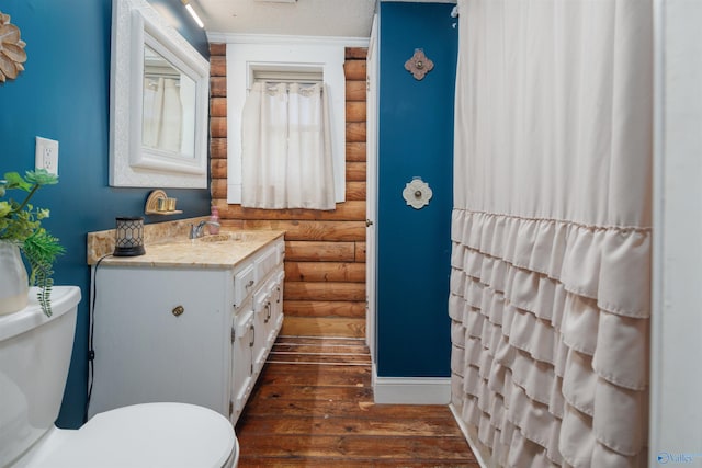 bathroom featuring a textured ceiling, wood-type flooring, toilet, rustic walls, and vanity