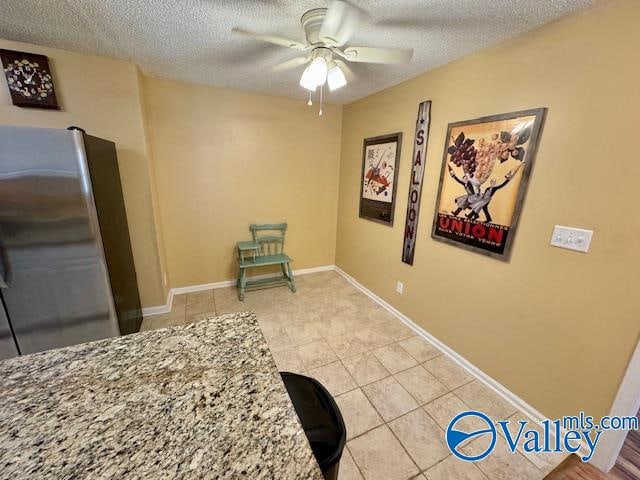 interior space featuring light tile patterned flooring, ceiling fan, stainless steel refrigerator, and a textured ceiling