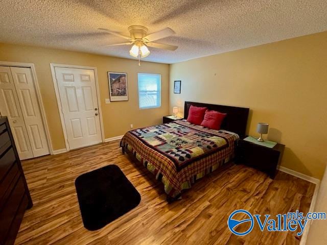 bedroom featuring a textured ceiling, ceiling fan, multiple closets, and light hardwood / wood-style flooring