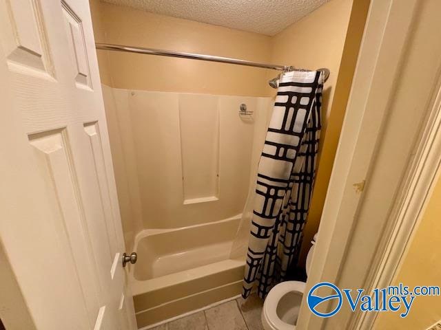 bathroom with tile patterned flooring, shower / bathtub combination with curtain, a textured ceiling, and toilet