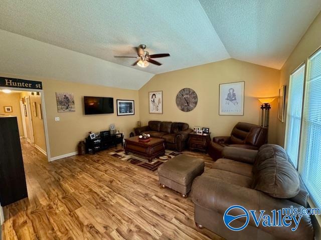 living room with wood-type flooring, vaulted ceiling, a textured ceiling, and ceiling fan