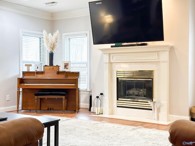 living room with baseboards, a fireplace with flush hearth, wood finished floors, and crown molding